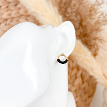 Load image into Gallery viewer, Gold and black circular earring on a white stand with a blurred beige background