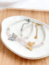 Load image into Gallery viewer, Two butterfly-themed bracelets on a white dish with a wooden background