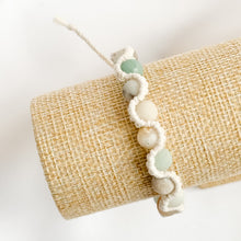Load image into Gallery viewer, Bracelet with white and green beads on a beige woven clutch against a white background
