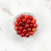Load image into Gallery viewer, Clear container filled with red and orange beads on a white marble surface
