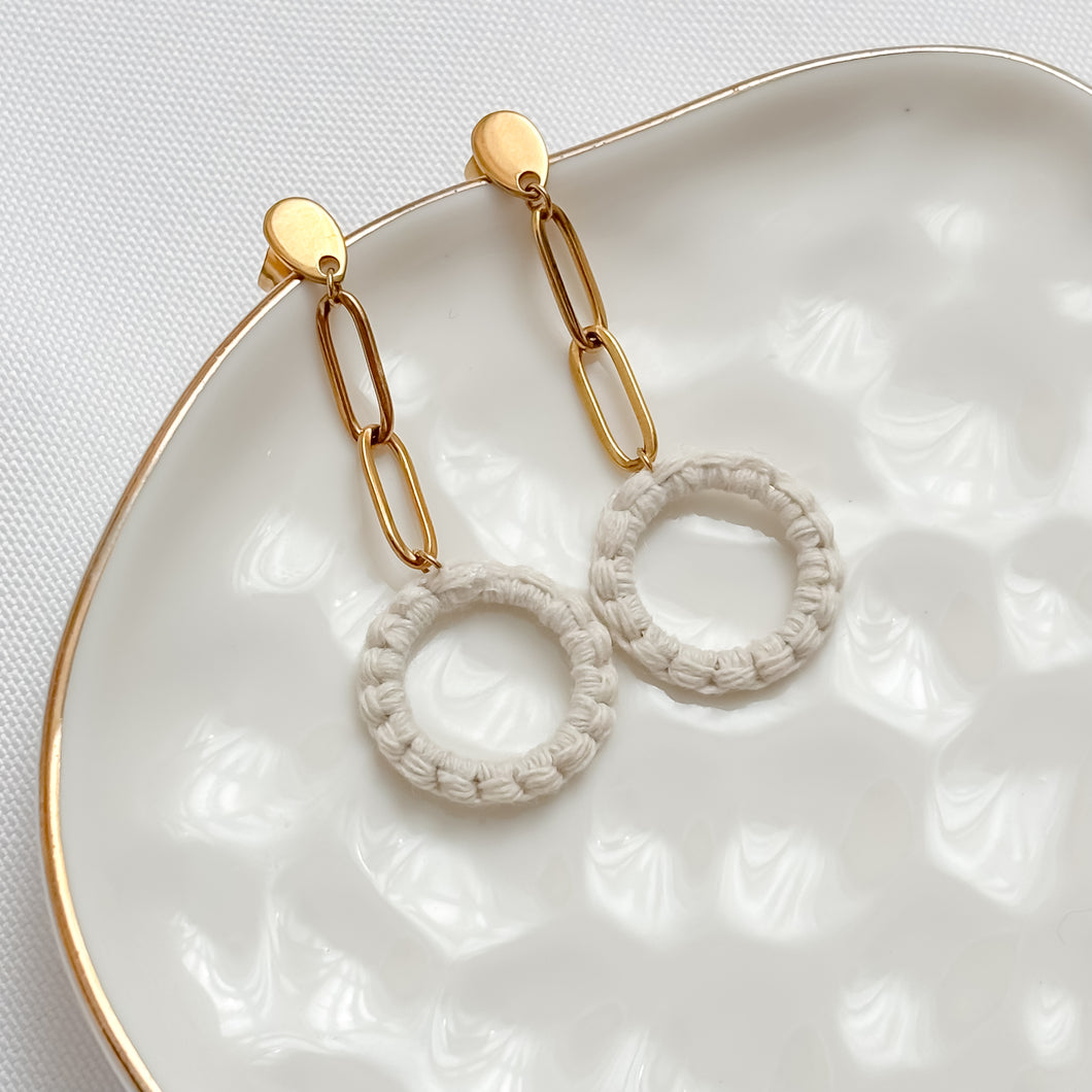 Gold chain earrings with circular designs on a textured white dish