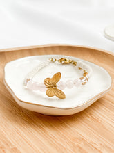 Load image into Gallery viewer, Gold butterfly bracelet on a white dish with a wooden surface
