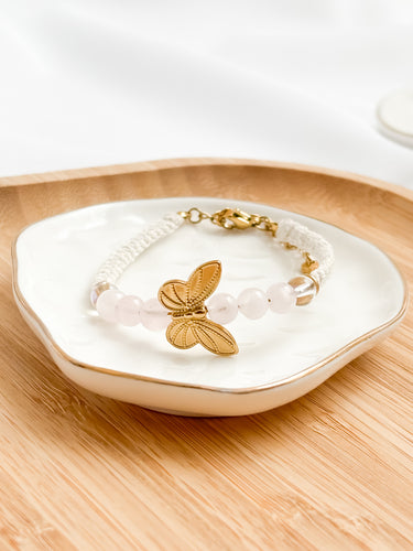 Gold butterfly bracelet on a white dish with a wooden surface