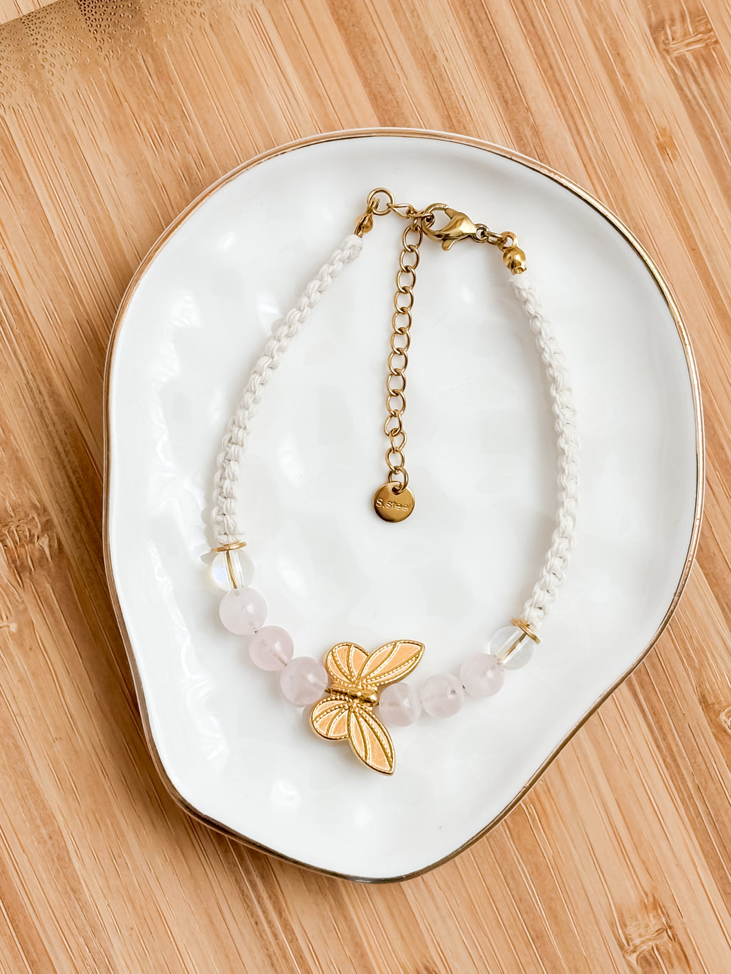 Bracelet with butterfly charm on a white dish on a wooden surface