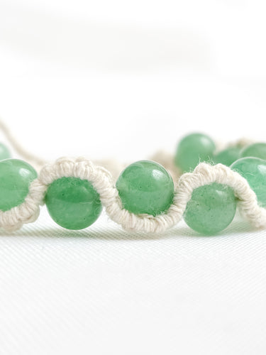 Green beaded bracelet with white macrame cord on a white background