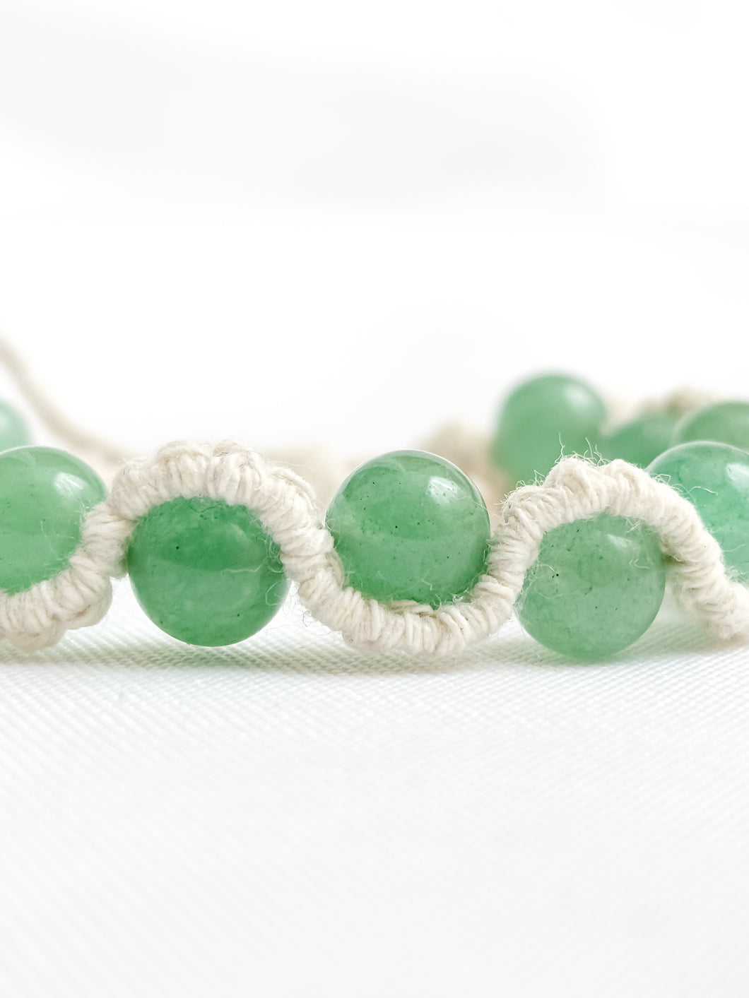 Green beaded bracelet with white macrame cord on a white background