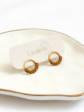 Load image into Gallery viewer, Gold hoop earrings on a white dish with &#39;Limitless&#39; branding.
