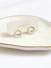 Load image into Gallery viewer, Gold and white earrings on a &#39;Limilless&#39; branded stand with a white background
