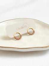 Load image into Gallery viewer, Gold hoop earrings on a white dish with &#39;Limitless&#39; branding.
