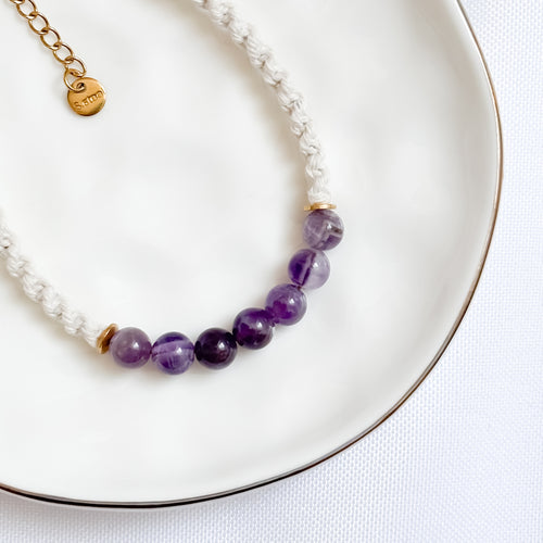 Bracelet with purple beads and gold chain on a white plate