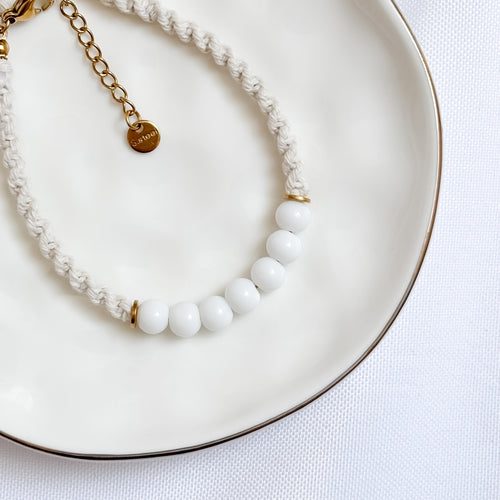 Bracelet with white beads and gold chain on a white plate
